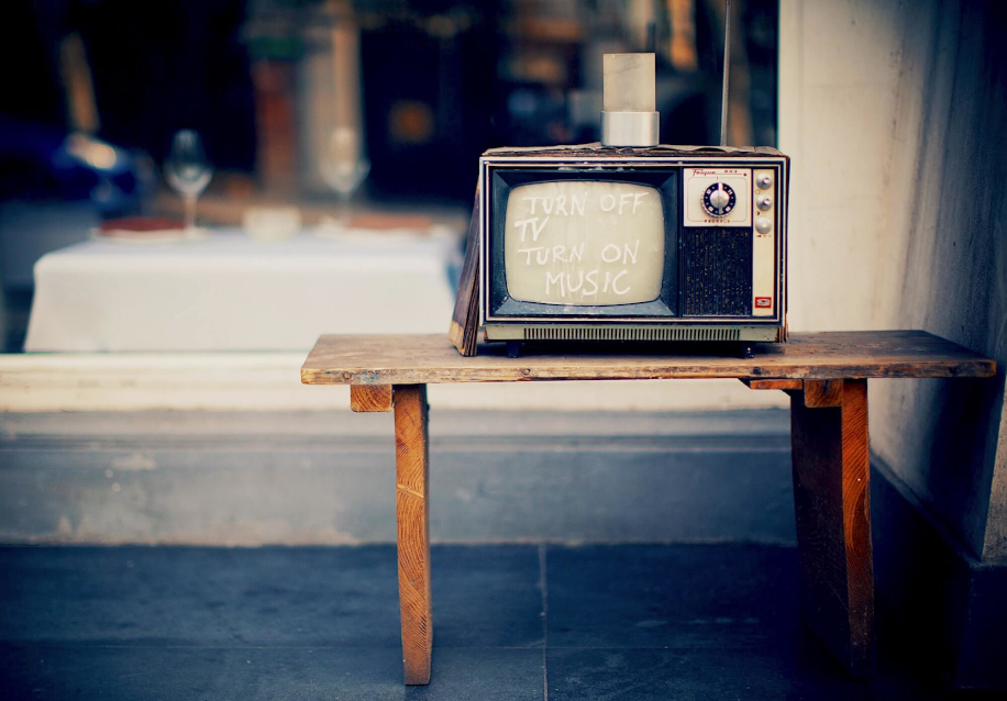 Ретро-телевизор с надписью «TURN OFF TV TURN ON MUSIC», стоящий на уличном столе