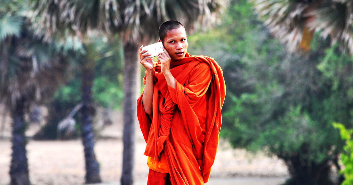 Юный буддийский монах слушает музыку через смартфон, приложив его к уху