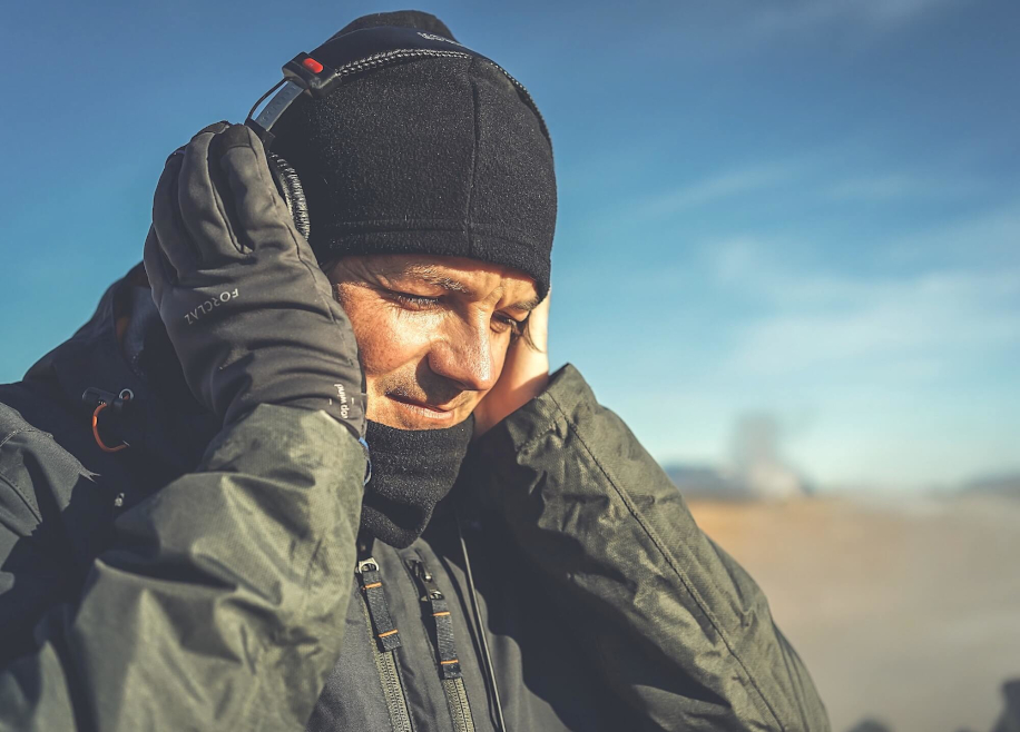 Мужчина в холодную погоду придерживает руками надетые на голову беспроводные наушники