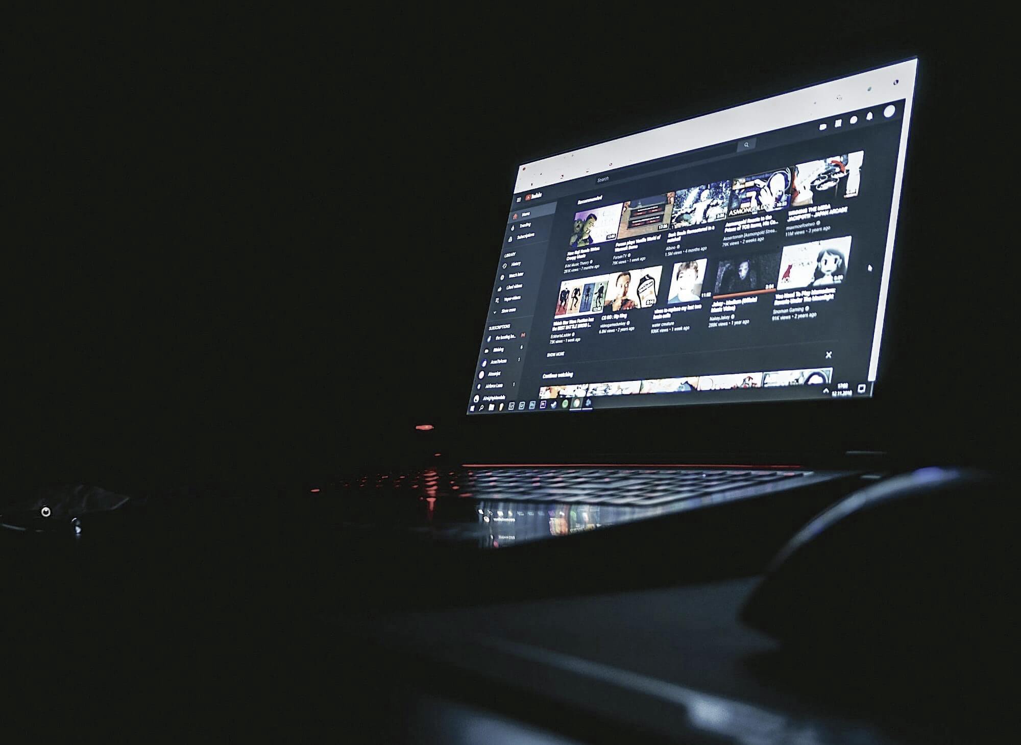 Экран ноутбука в темноте, на котором отображается страничка видеохостинга YouTube