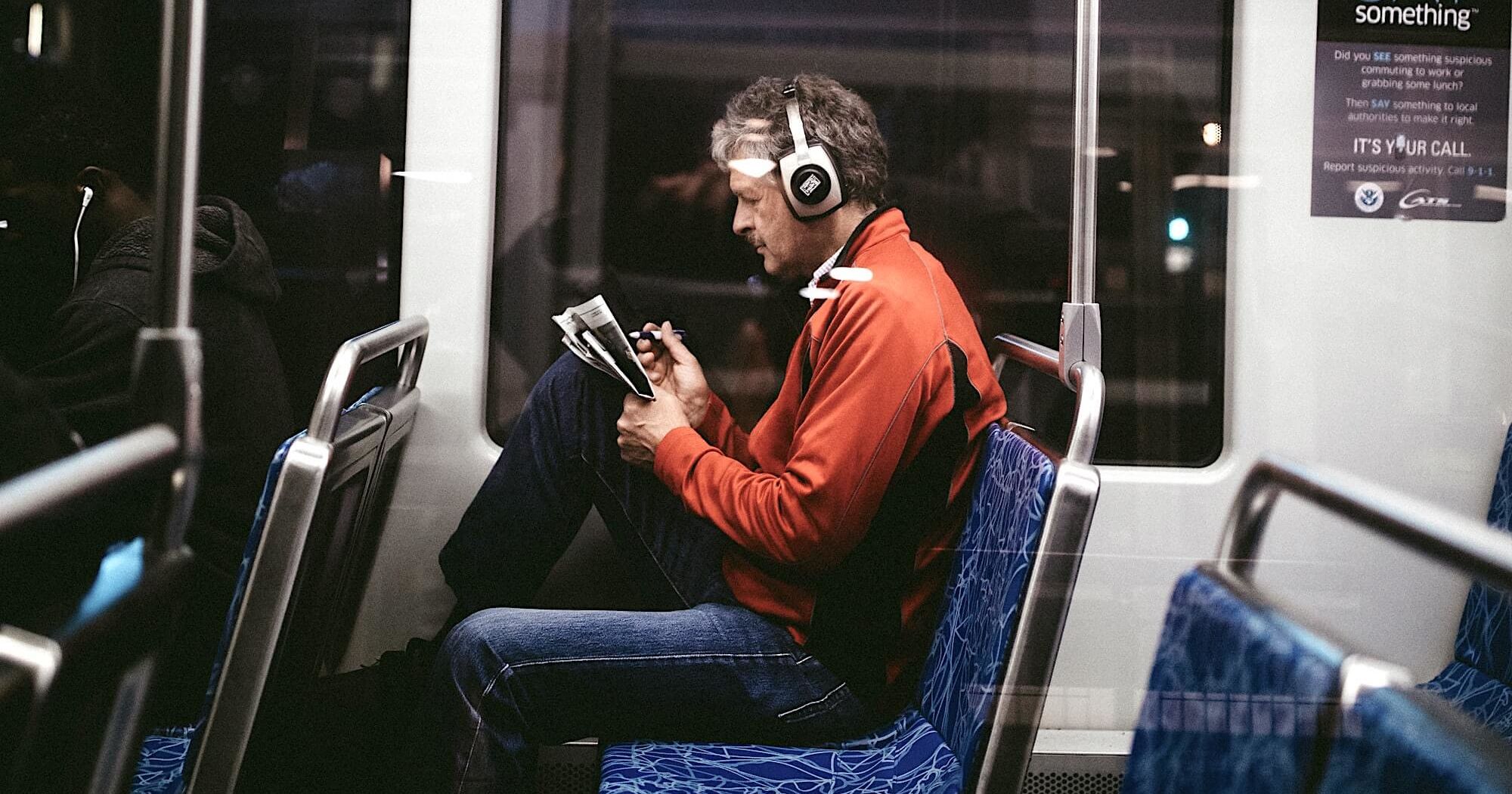 Мужчина в наушниках, едущий в общественном транспорте, читает газету