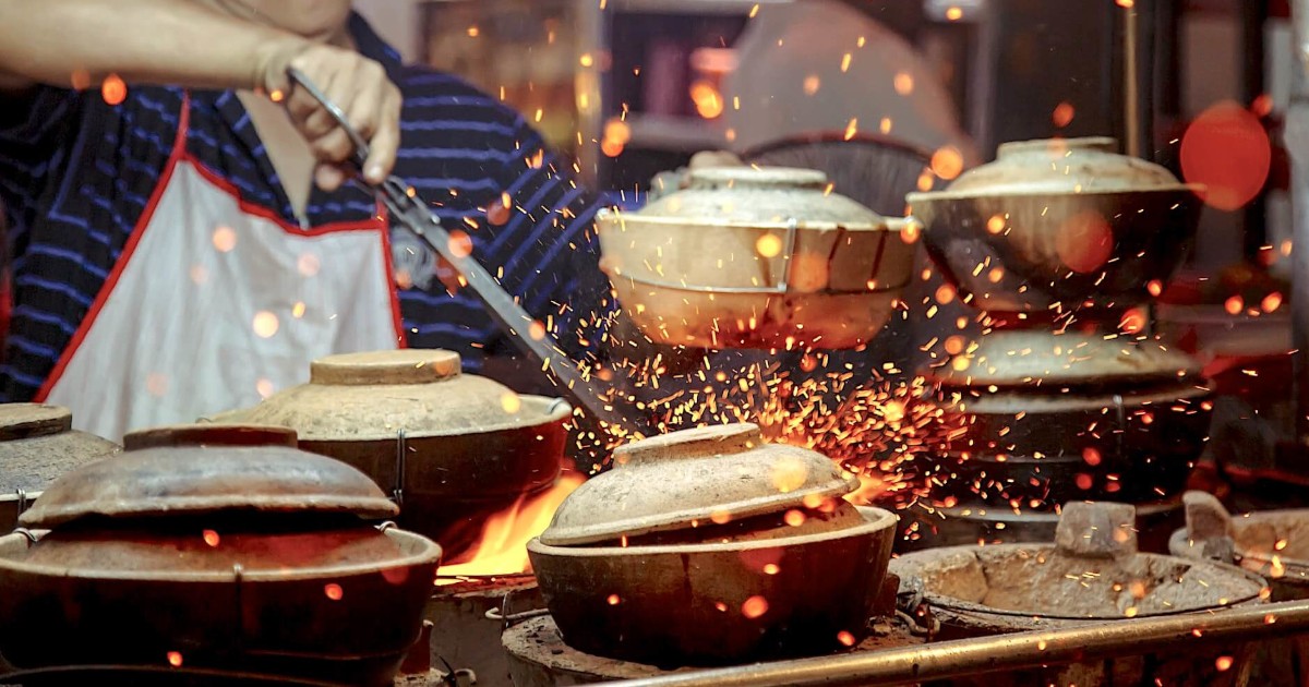 Азиатский повар орудует с горячими горшками при помощи щипцов