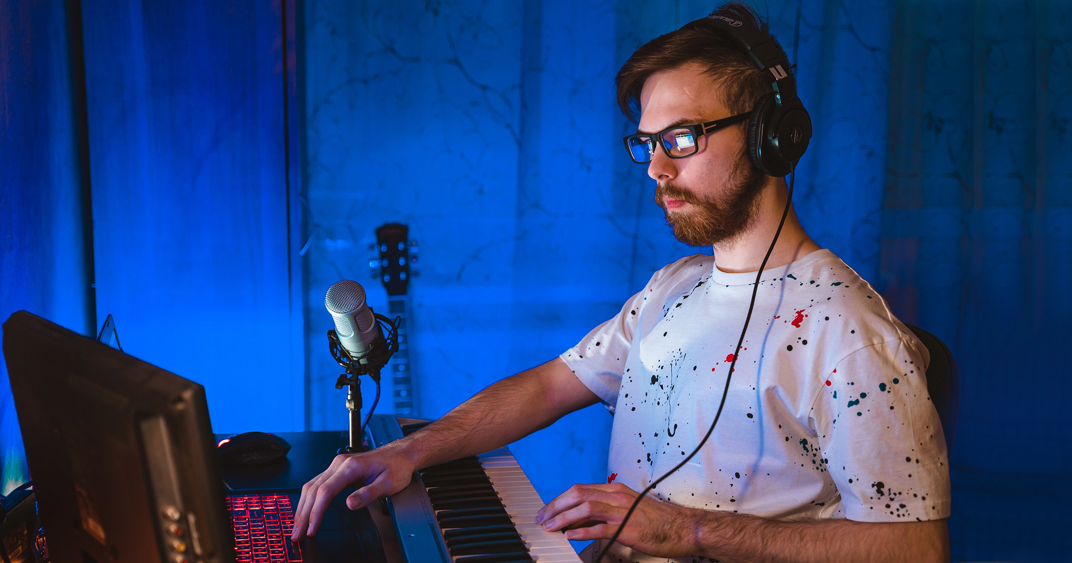 Мужчина в очках деалет семплы с клавишных, сидя на фоне синей шторы