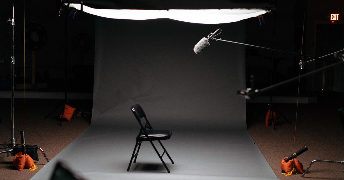 Студия с выставленным светом и подвесным микрофоном, расположенным над пустующим стулом
