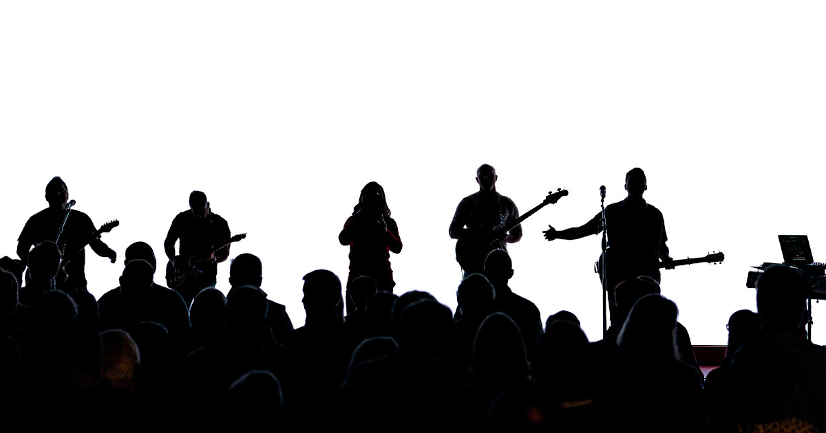 Силуэты группы, выступающей на сцене перед публикой в зале