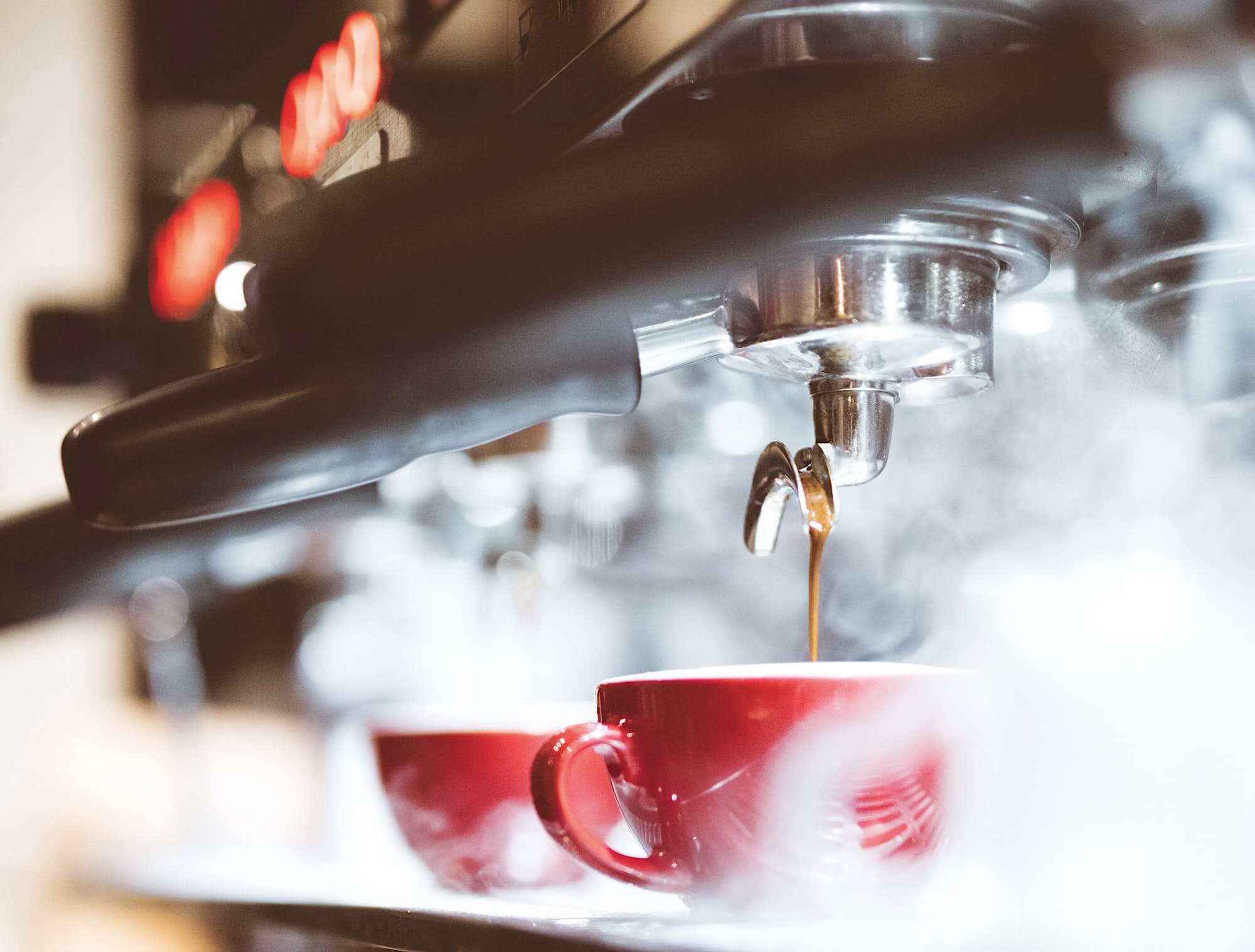Приготовление капучино ресторанной кофе-машиной, разливающей напиток в красные чашки