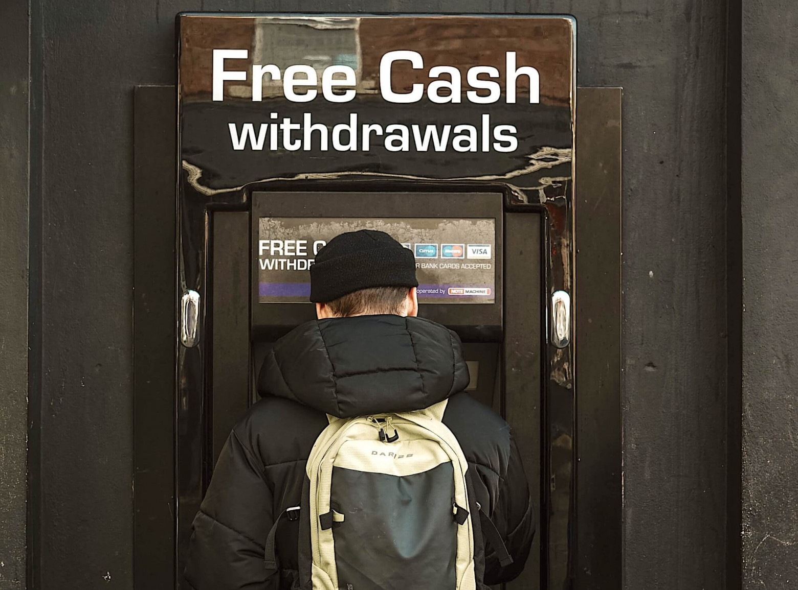 Мужчина, снимающий деньги в банкомате с вывеской «Бесплатное снятие наличных»