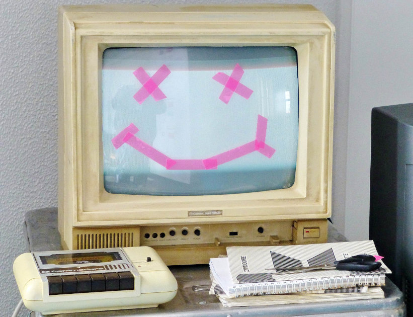 ЭЛТ-монитор с «мёртвым» смайликом из стикеров на экране, стоящий на столе рядом с кассетным плеером и канцтоварами
