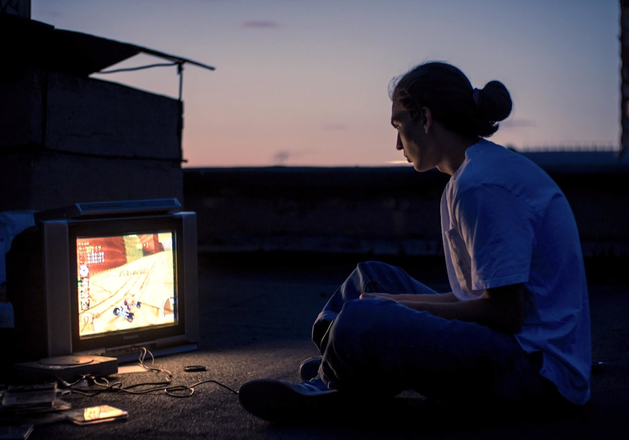 Геймер играет при помощи консоли и телевизора на открытом воздухе в сумерках