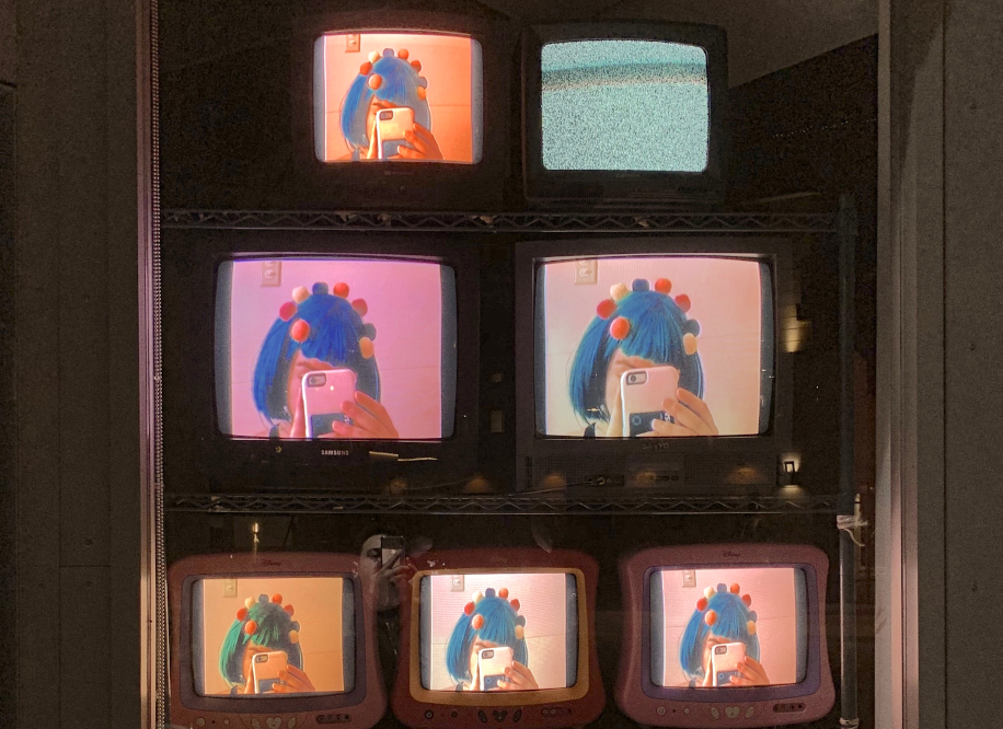 Изображение делающей селфи девушки, воспроизводящееся на нескольких телевизорах за витриной