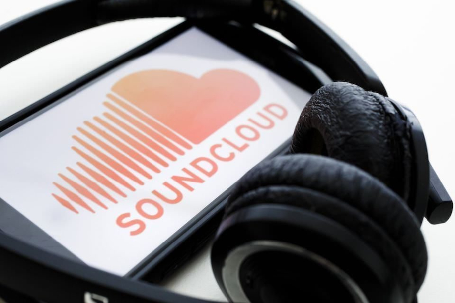 Смартфон с логотипом SoundCloud на экране, лежащий в обрамлении накладных наушников