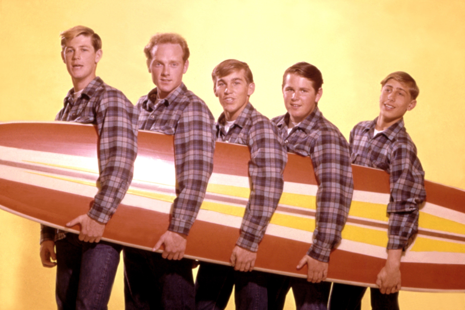 Коллектив группы The Beach Boys (экс-The Pendletones) в рубашках Пендлтон позирует для фото с доской для серфинга. Август 1962, Лос-Анджелес, Калифорния, США