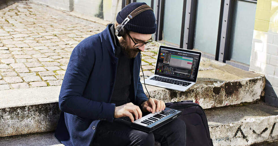 Мужчина в наушниках, сидящий на уличных ступеньках с MIDI-клавиатурой Nektar Impact GX Mini