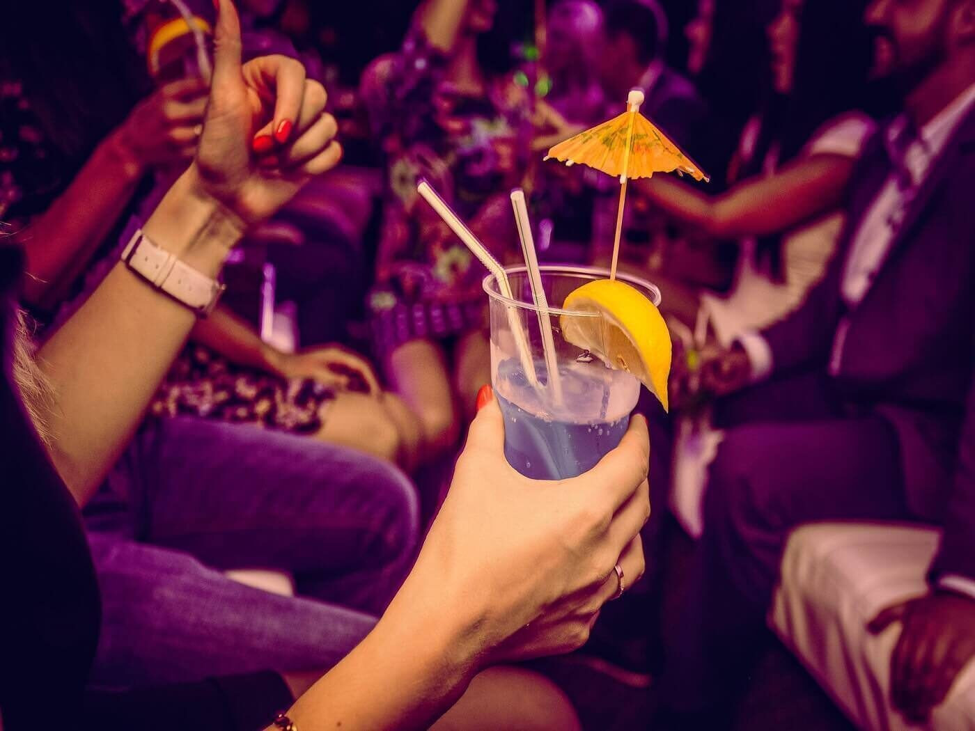 Стакан с коктейлем в руке девушки, тусующейся в ночном клубе